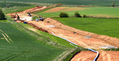 Newfield Project Progress Construction site in a rural area with machinery working on a large trench surrounded by green fields.